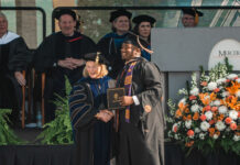 Mercer scholar-athlete Bears post record year in the classroom Graduate in cap and gown shakes hands with faculty member on stage at a commencement ceremony with flowers nearby.