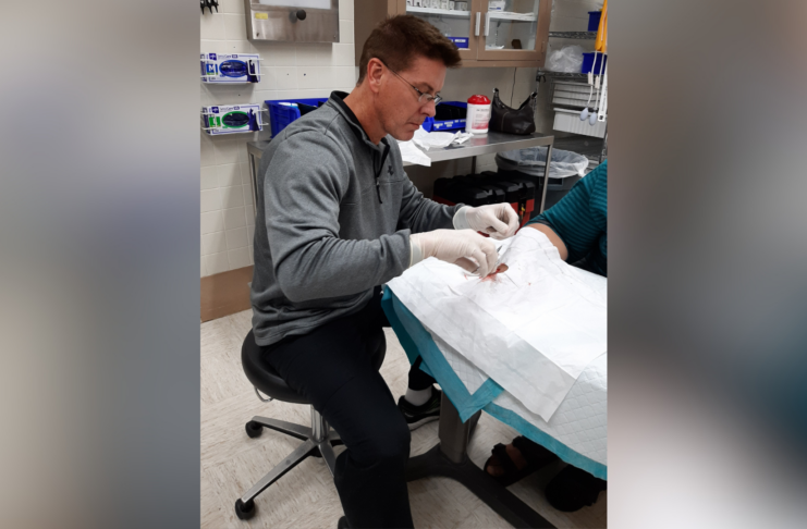 A medical professional in gloves sutures a patients hand in a clinical setting.