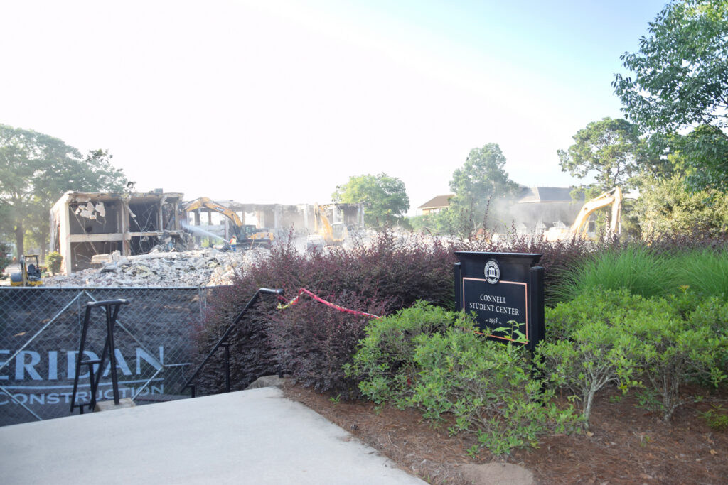 Demolition equipment tearing down a building behind a sign reading Connell Student Center and construction fencing.