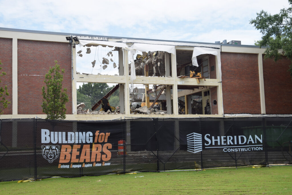 A partially demolished brick building behind a construction fence with signs for Sheridan Construction and Building for Bears.