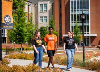 Class of 2026 graduates offer this advice to incoming students Three students walk and talk on a college campus sidewalk near a Be the Bear banner and brick buildings.