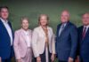 School of Medicine and Tanner Health celebrate opening of Carrollton Clinical Campus and Simulation Lab Five professionally dressed adults stand side by side against a green and red backdrop, facing the camera.