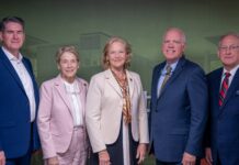 School of Medicine and Tanner Health celebrate opening of Carrollton Clinical Campus and Simulation Lab Five professionally dressed adults stand side by side against a green and red backdrop, facing the camera.
