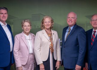 School of Medicine and Tanner Health celebrate opening of Carrollton Clinical Campus and Simulation Lab Five professionally dressed adults stand side by side against a green and red backdrop, facing the camera.