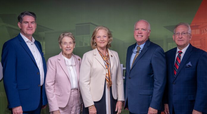 School of Medicine and Tanner Health celebrate opening of Carrollton Clinical Campus and Simulation Lab Five professionally dressed adults stand side by side against a green and red backdrop, facing the camera.