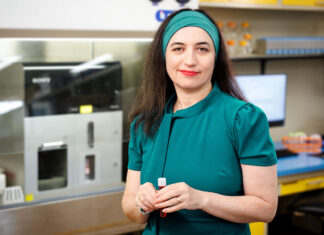 Mercer School of Medicine awarded $100,000 cancer research grant Dr. Chefetz Menaker in teal dress holding a small tube while standing in the laboratory where her research will take place.