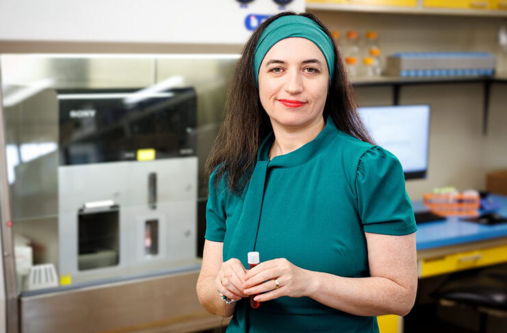 Dr. Chefetz Menaker in teal dress holding a small tube while standing in the laboratory where her research will take place.