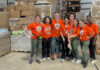 Mercer family therapy students provide behavioral healthcare to farmworkers MUSM team in matching orange shirts stand and smile in a warehouse with boxes and pallets in the background.