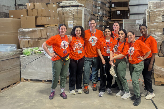 MUSM team in matching orange shirts stand and smile in a warehouse with boxes and pallets in the background.