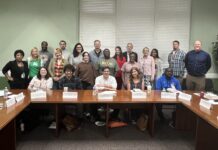 Mercer helps teachers bring student-centered discussions to their classrooms A group of adults pose for a photo in a conference room, seated and standing around wooden tables with nameplates.