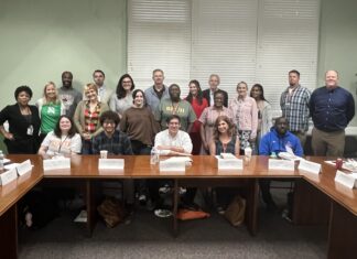 Mercer helps teachers bring student-centered discussions to their classrooms A group of adults pose for a photo in a conference room, seated and standing around wooden tables with nameplates.
