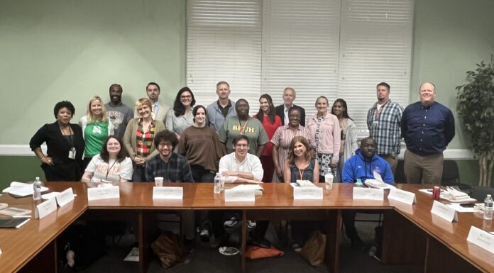 Mercer helps teachers bring student-centered discussions to their classrooms A group of adults pose for a photo in a conference room, seated and standing around wooden tables with nameplates.
