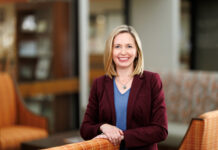 School of Medicine alumna continues tradition of mentorship as associate dean for student affairs Woman in a maroon blazer and blue shirt smiles while standing in a modern, warmly lit office lounge area.