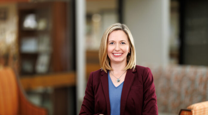 School of Medicine alumna continues tradition of mentorship as associate dean for student affairs Woman in a maroon blazer and blue shirt smiles while standing in a modern, warmly lit office lounge area.