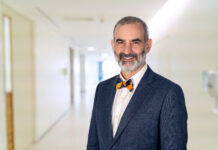 School of Medicine names Dr. Matthew Varn as Valdosta campus associate dean Dr. Matt Varn in a blue suit and bow tie standing and smiling in a brightly lit hallway.