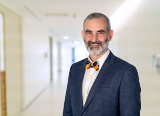 School of Medicine names Dr. Matthew Varn as Valdosta campus associate dean Dr. Matt Varn in a blue suit and bow tie standing and smiling in a brightly lit hallway.