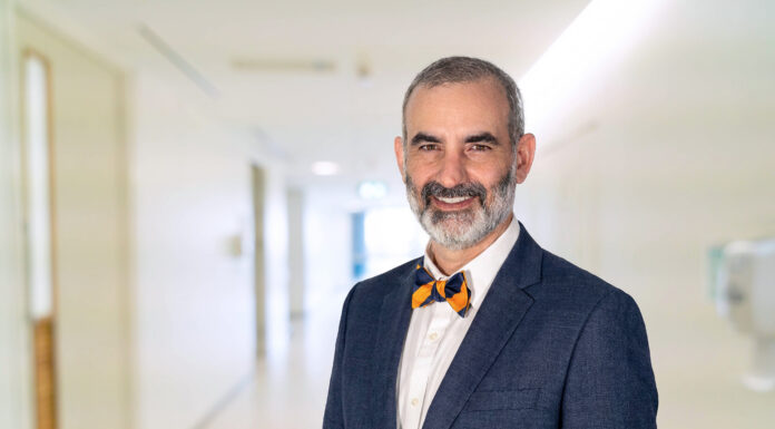 School of Medicine names Dr. Matthew Varn as Valdosta campus associate dean Dr. Matt Varn in a blue suit and bow tie standing and smiling in a brightly lit hallway.