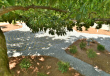 What are you listening to? | Dr. Greg DeLoach A stone labyrinth is visible beneath tree branches, surrounded by shrubs and pine straw in a garden setting.