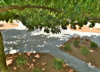 What are you listening to? | Dr. Greg DeLoach A stone labyrinth is visible beneath tree branches, surrounded by shrubs and pine straw in a garden setting.