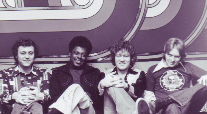 Alan Walden’s influence reached from Mercer to Macon and beyond Four men sitting on a patterned couch in front of a geometric backdrop, all facing the camera and smiling.