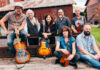Amy Ray of Indigo Girls kicks off Mercer series exploring Southern music Seven people with musical instruments pose outdoors in front of a rustic barn and metal fence.
