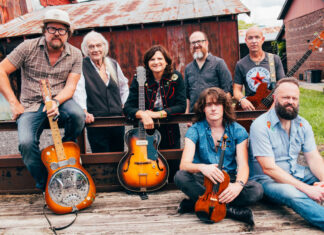 Amy Ray of Indigo Girls kicks off Mercer series exploring Southern music Seven people with musical instruments pose outdoors in front of a rustic barn and metal fence.