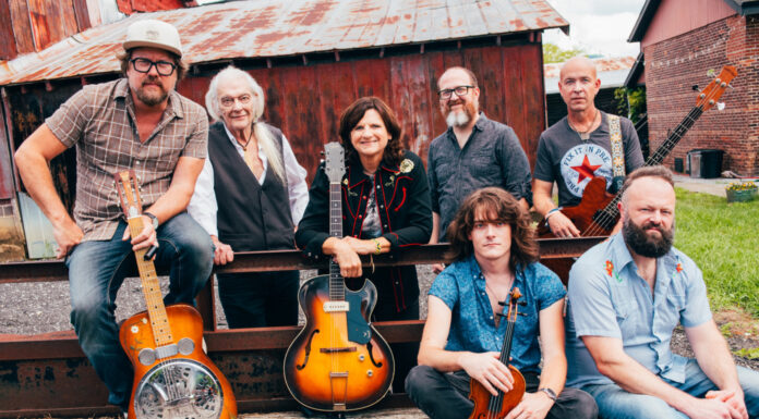Amy Ray of Indigo Girls kicks off Mercer series exploring Southern music Seven people with musical instruments pose outdoors in front of a rustic barn and metal fence.