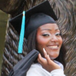 Person smiling in graduation cap and gown, holding the gown over their shoulder, standing outdoors.