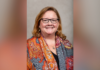 Dr. Sharon Augustine appointed interim dean of Tift College of Education Woman with glasses and long hair, smiling, wearing an orange patterned scarf over a dark top, in front of a neutral background.