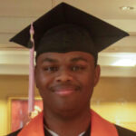 A person wearing a black graduation cap and gown with an orange stole, smiling at the camera indoors.