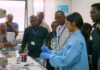 Mercer On Mission program in Kenya teaches low-cost method to test for lead in paint A group of people observe a scientist in a lab coat and gloves demonstrating an experiment in a laboratory.