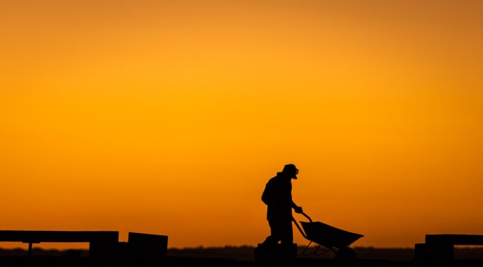 Professor developing tool to address heat stress Silhouette of a person pushing a wheelbarrow at sunset, with an orange sky in the background.