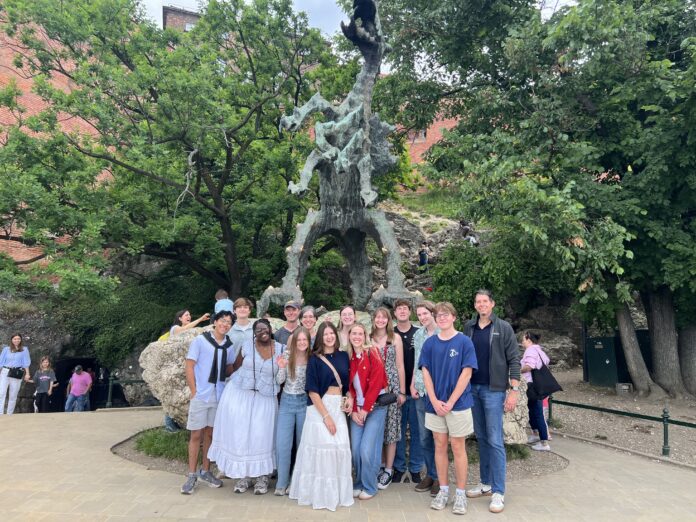 A group of people pose in front of a large outdoor dragon statue surrounded by trees and rocky terrain.