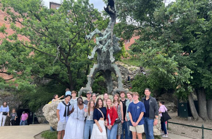 A group of people pose in front of a large outdoor dragon statue surrounded by trees and rocky terrain.