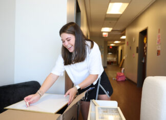 Wandering your way home | Greg DeLoach, D.Min. A Mercer student unpacks a box in a hallway, surrounded by moving boxes and furniture.