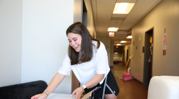 Wandering your way home | Greg DeLoach, D.Min. A Mercer student unpacks a box in a hallway, surrounded by moving boxes and furniture.