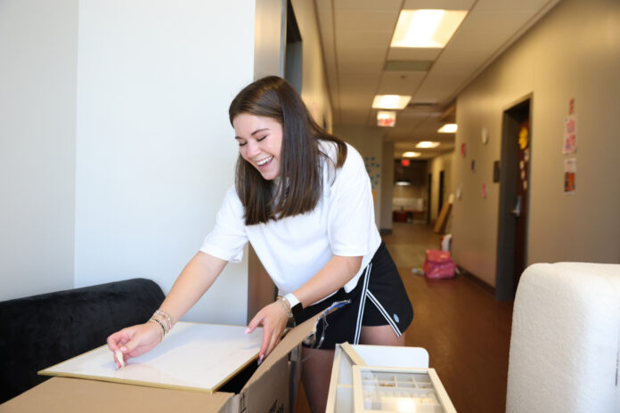 A Mercer student unpacks a box in a hallway, surrounded by moving boxes and furniture.