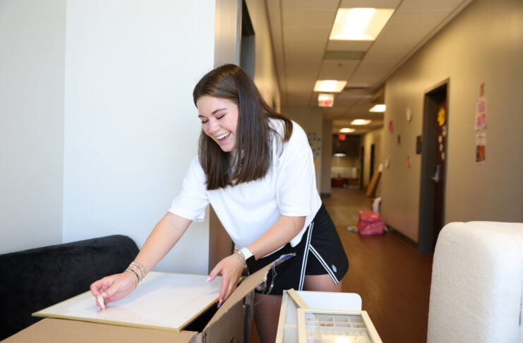 A Mercer student unpacks a box in a hallway, surrounded by moving boxes and furniture.