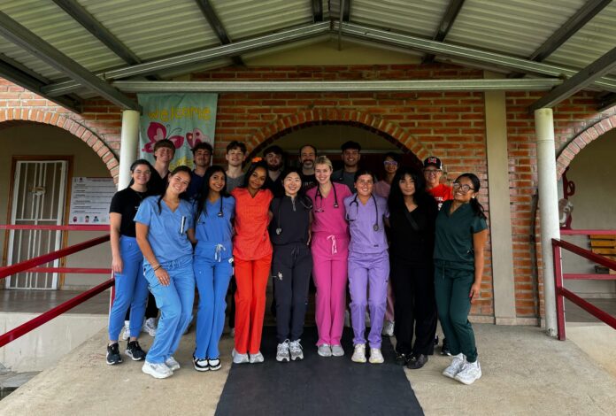 Honduras medical group A group of people in colorful scrubs stands together under a covered walkway in front of a brick building.