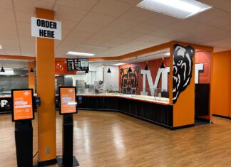 What’s new with Atlanta campus dining this year Fast food restaurant interior with self-order kiosks, serving counter, and bear mascot wall art.