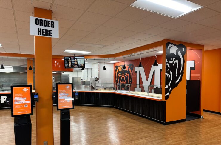 Fast food restaurant interior with self-order kiosks, serving counter, and bear mascot wall art.
