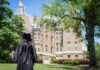 Mercer one of Princeton Review’s ‘Best Colleges’ for 24th consecutive year A graduate in cap and gown stands on grass facing a large, historic brick building surrounded by trees.