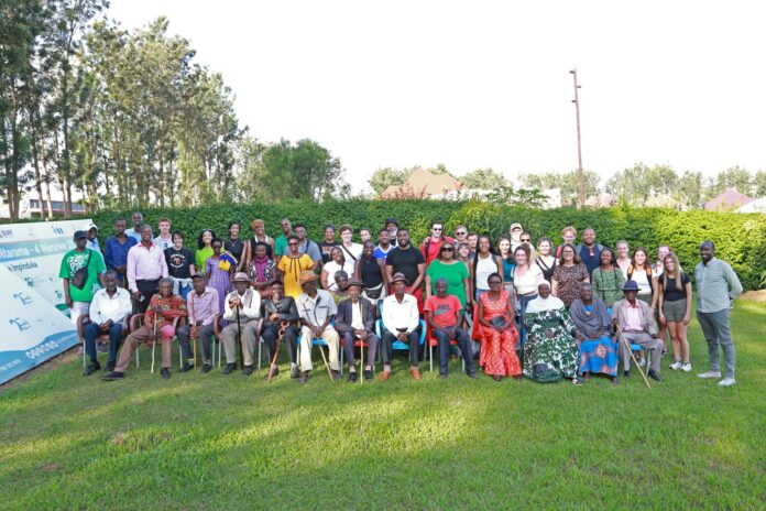 A large group of people pose for a photo outdoors on grass, with trees and bushes in the background.