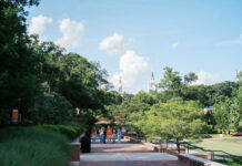 Faculty and Staff Notables | September 2026 Four people walk on a tree-lined brick path with two white church steeples visible in the background under a blue sky.