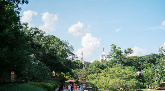 Faculty and Staff Notables | September 2026 Four people walk on a tree-lined brick path with two white church steeples visible in the background under a blue sky.