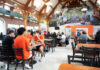 What’s new with Mercer dining for fall 2026 Students sit and talk in a busy university dining hall with wooden beams and a large mural on the back wall.