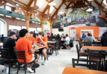 What’s new with Mercer dining for fall 2026 Students sit and talk in a busy university dining hall with wooden beams and a large mural on the back wall.