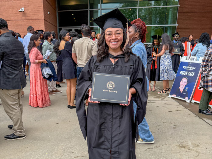 Alicia Hernandez holds a diploma outside a building, surrounded by people at a graduation ceremony.