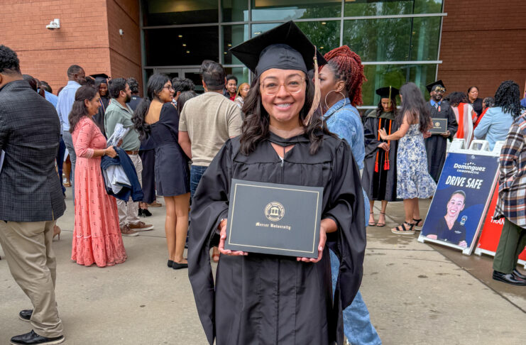 Alicia Hernandez holds a diploma outside a building, surrounded by people at a graduation ceremony.