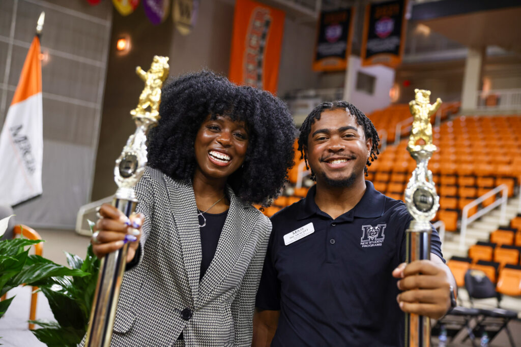 Two Mercer students smiling and holding maces in Hawkins Arena.